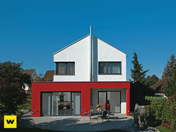 Modernes Einfamilienhaus mit roter Fassade und Garten bei blauem Himmel im Wohngebiet.