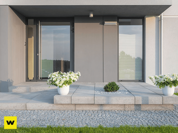 Moderner Hauseingang mit großen Fenstern, Pflanzkübeln und gepflegtem Eingangsbereich.