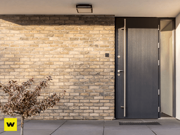 Moderne Haustür aus Aluminium vor heller Klinkerfassade mit stilvoller Außenbeleuchtung.